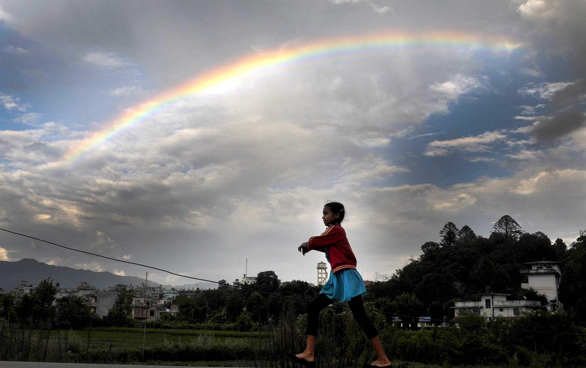 A young girl plays as a rainbow is seen on the monsoon sky in Kathmandu.