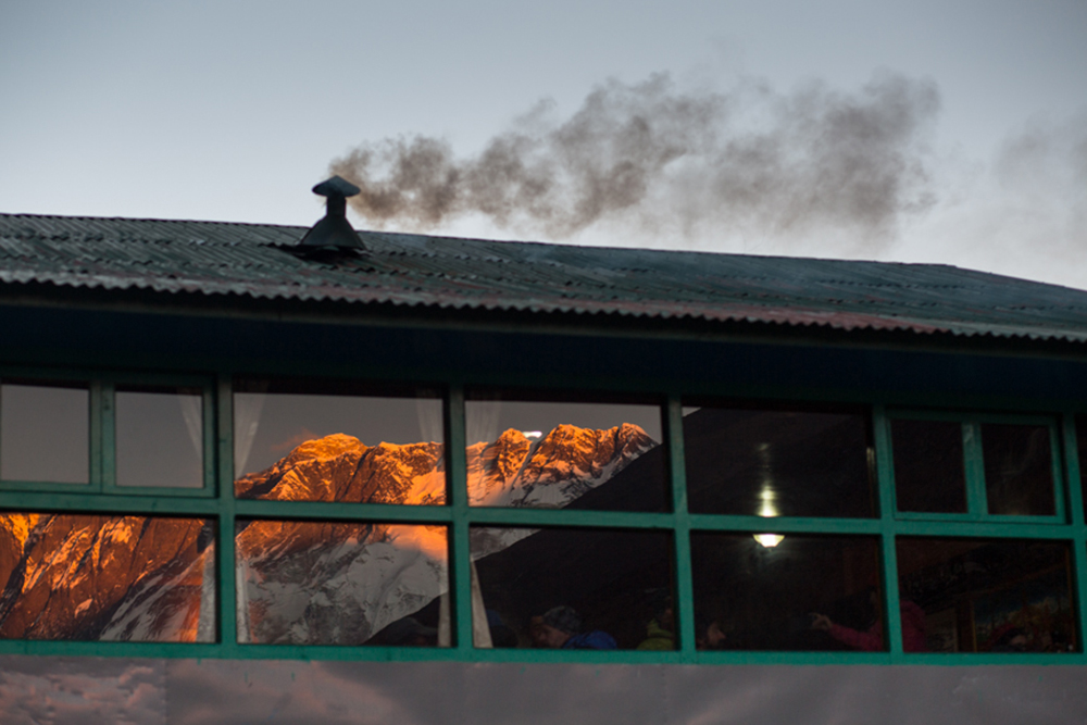 Smoke emited from a hotel in Debuche as the sun sets in Mt. Everest is reftected in the glass of dianning room. The smoke comes from the heating system for the dianning room. Recent study has shown that black carbon from such smoke is also cause for faster retreat of glaciers in Himalaya Region. Solukhumbu District, Nepal.