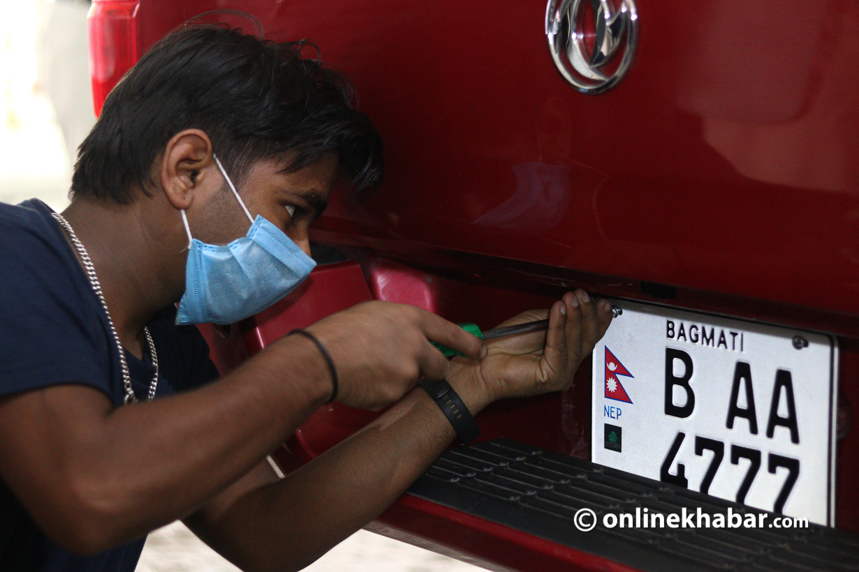 An embossed number plate is being installed on a vehicle.