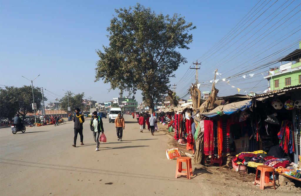 People walking by the shops on the roadside in the bus park area.